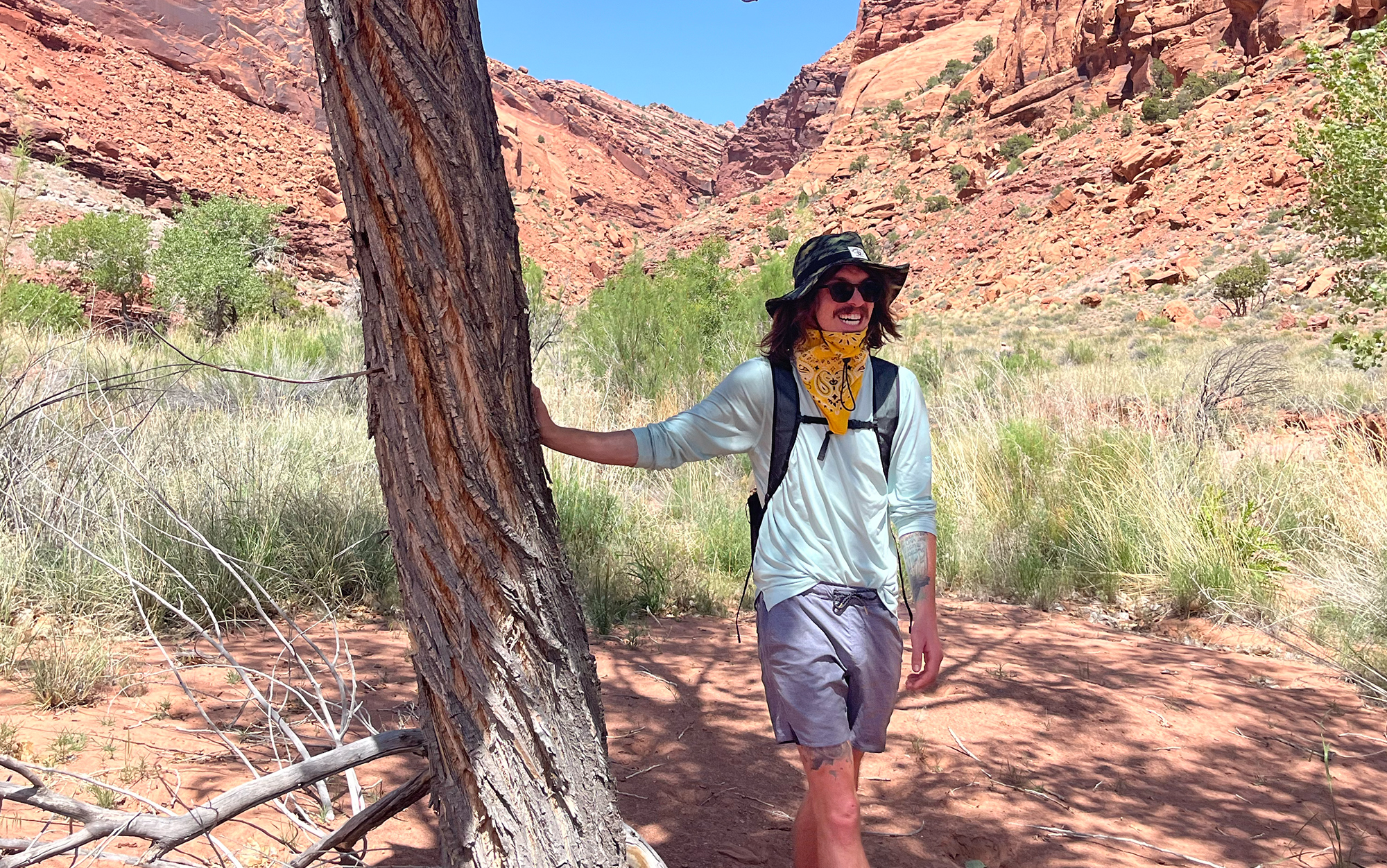 Hiker stands in the shade wearing a bandana and sun hat.