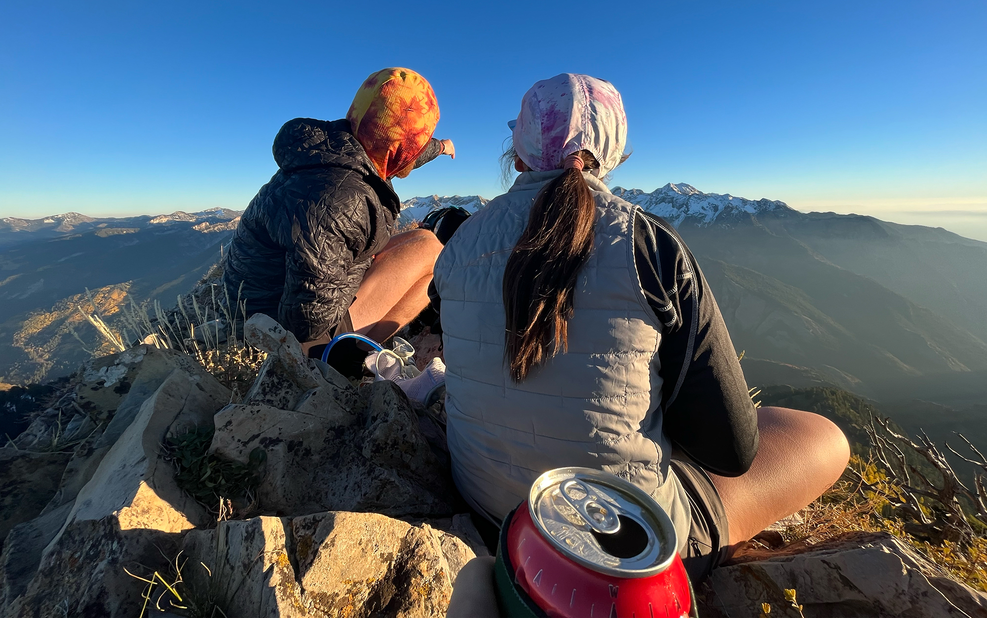 Hiker holds summit beer in front of two hiking partners.