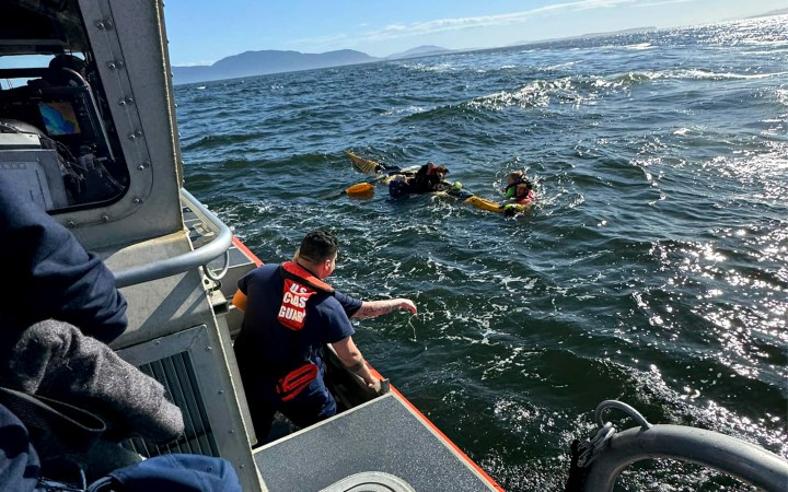 Coast guard rescuers pull sea kayakers from bay.