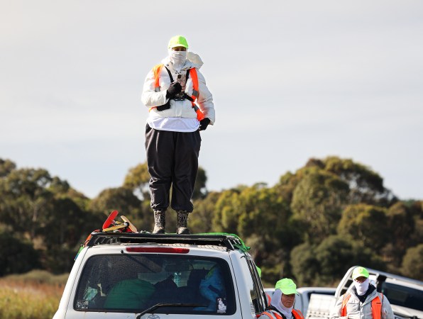 An anti-hunting activist in bright clothing stands on top of a vehicle at a public boat ramp in Australia.