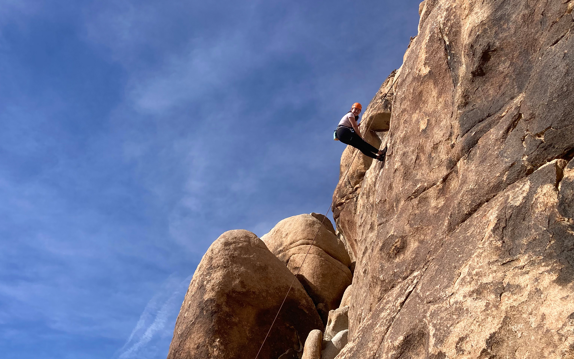 Climber hangs against a rock wall in Joshua Tree.
