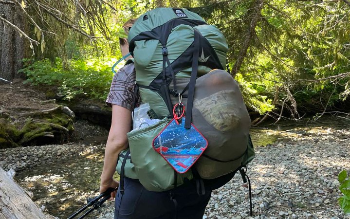  close up of granite gear backpack as a woman hikes across a log over a stream