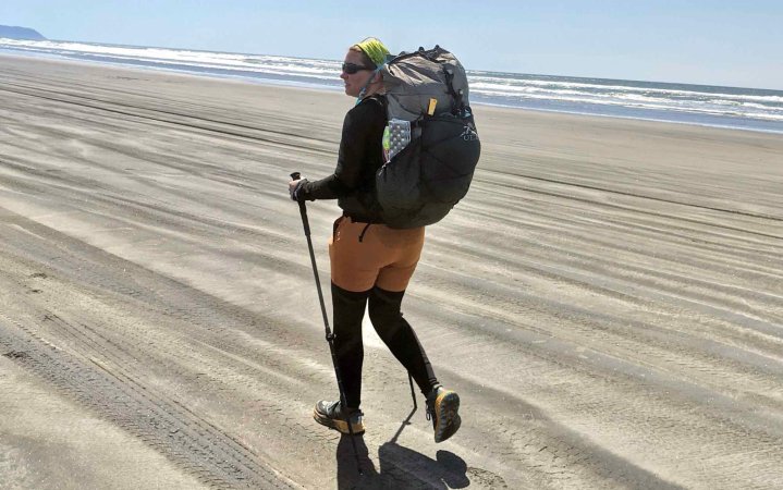  woman hiking on a beach wearing the ULA Circuit backpack