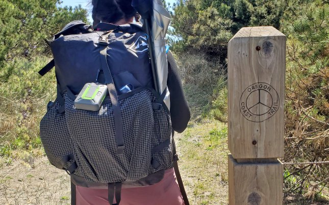 woman wearing hyperlite backpack next to oregon coast trail post