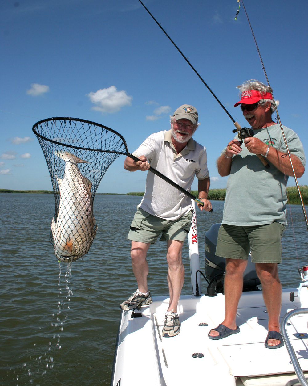 Two anglers hold up a redfish in a net.