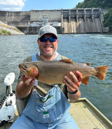 A smiling fisherman holds up a fat cutthroat trout.