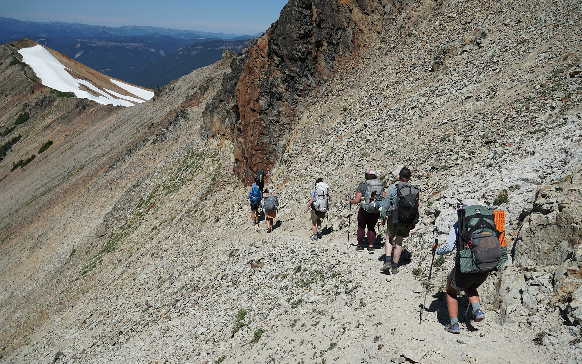 backpackers traverse a hillside using trekking poles.