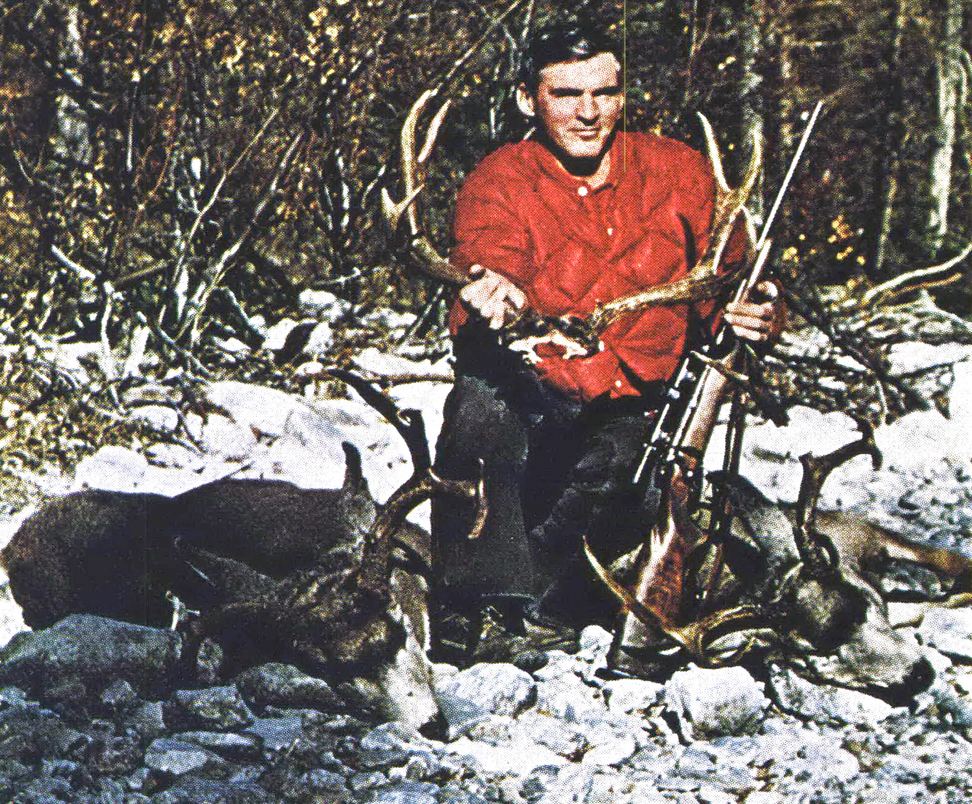 Bill McRae kneels besides two bucks while holding a mule deer rack in an old photo.