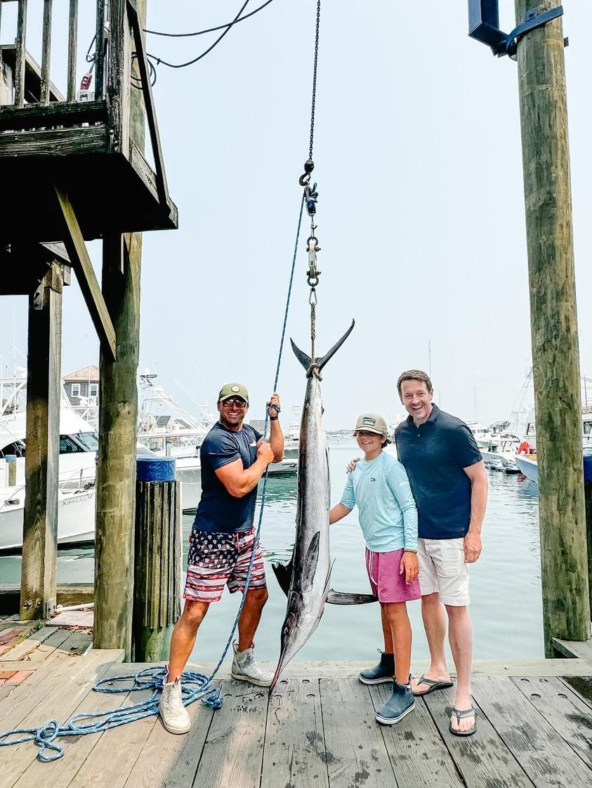 A kid with a white marlin and two adults on the dock.