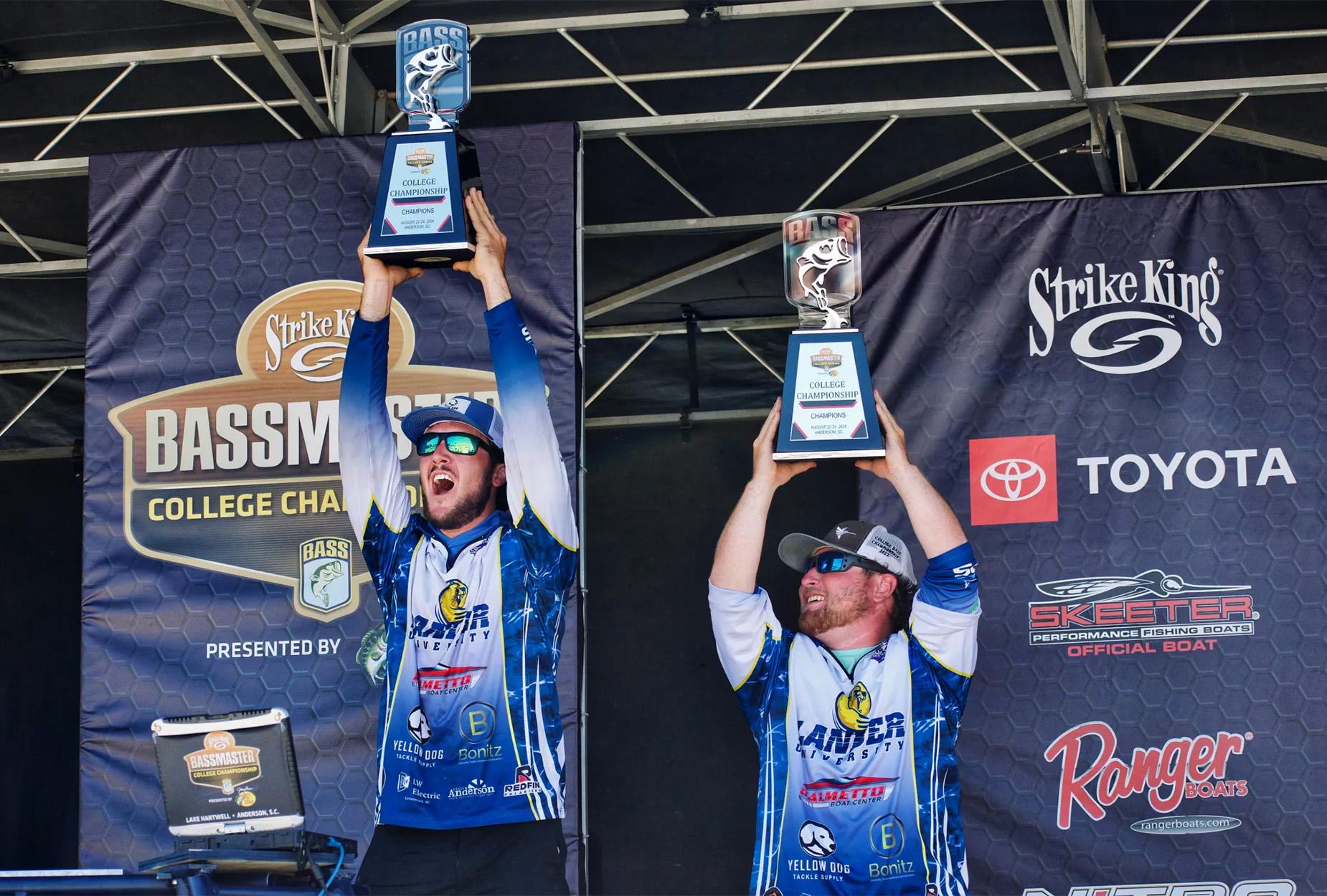 Two college bass fishermen hold up a trophy.