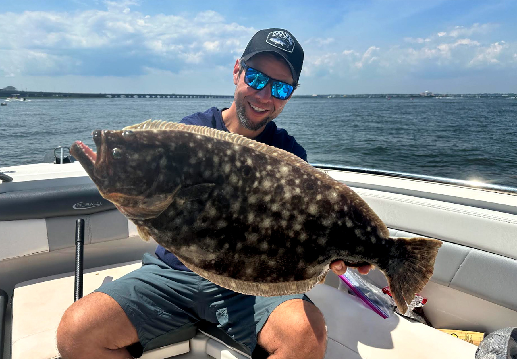 An angler holds up a flounder in a boat.