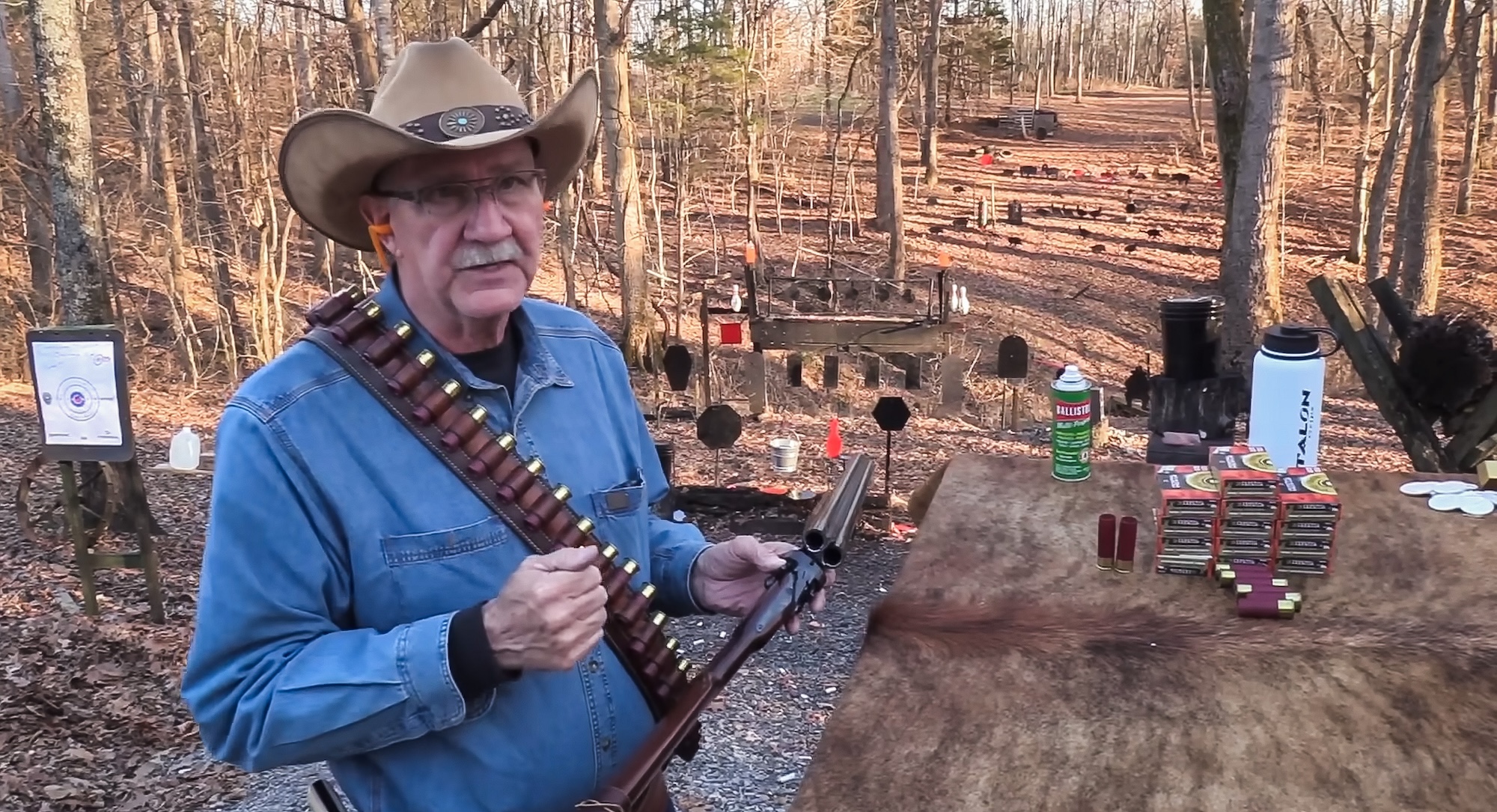 Hickock45 stands holding a coach gun on a steel target range.