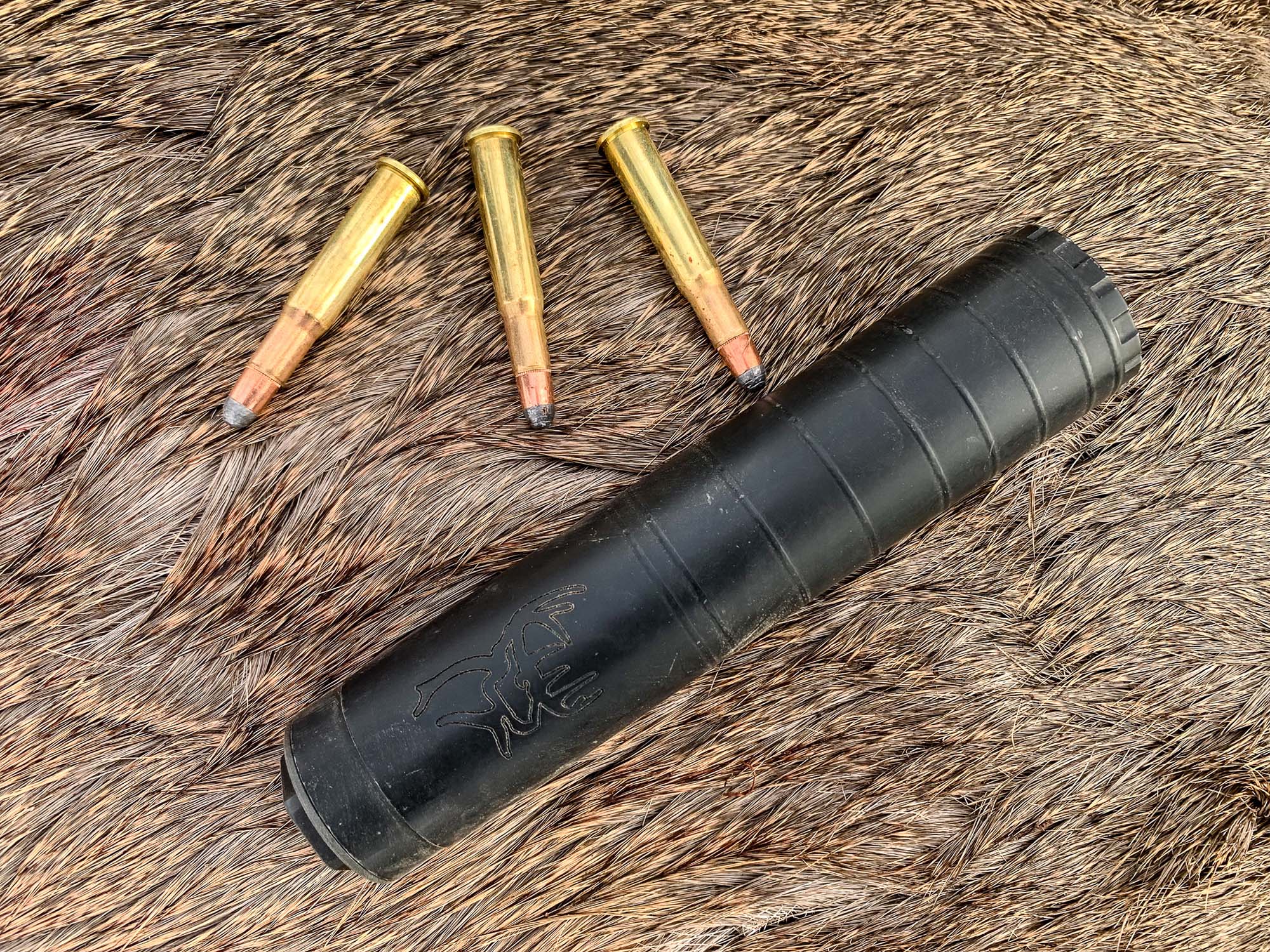 A Buck 30 suppressor on a deer hide with three 30/30 cartridges on top.