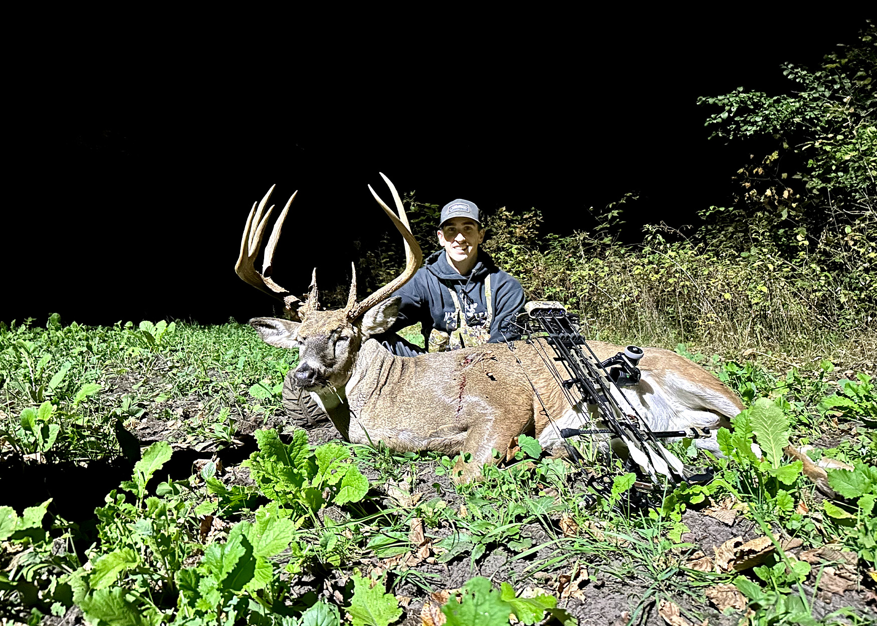 A bowhunter with buck in a bean field.