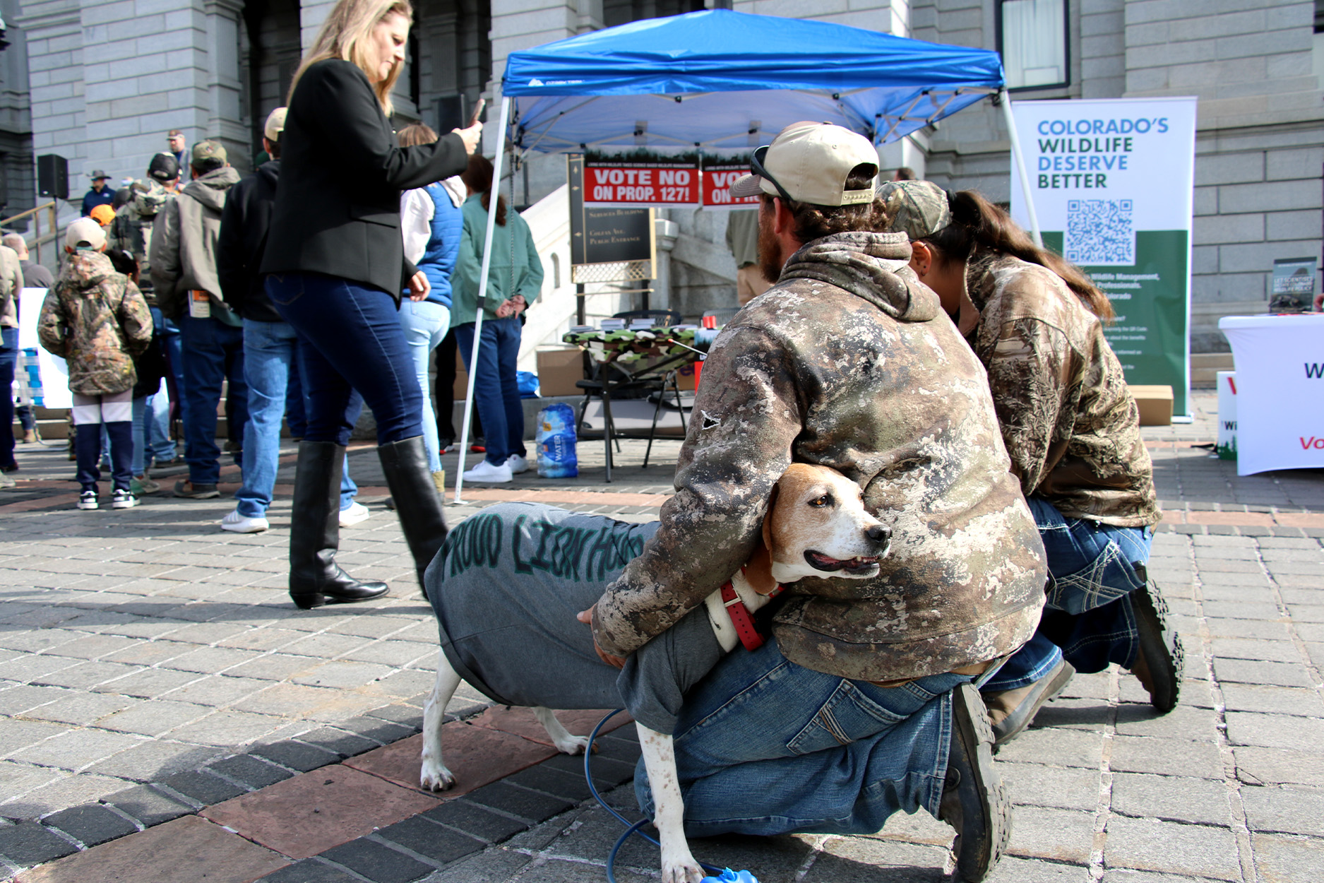 A hunter and his dog kneel behind a crowd.