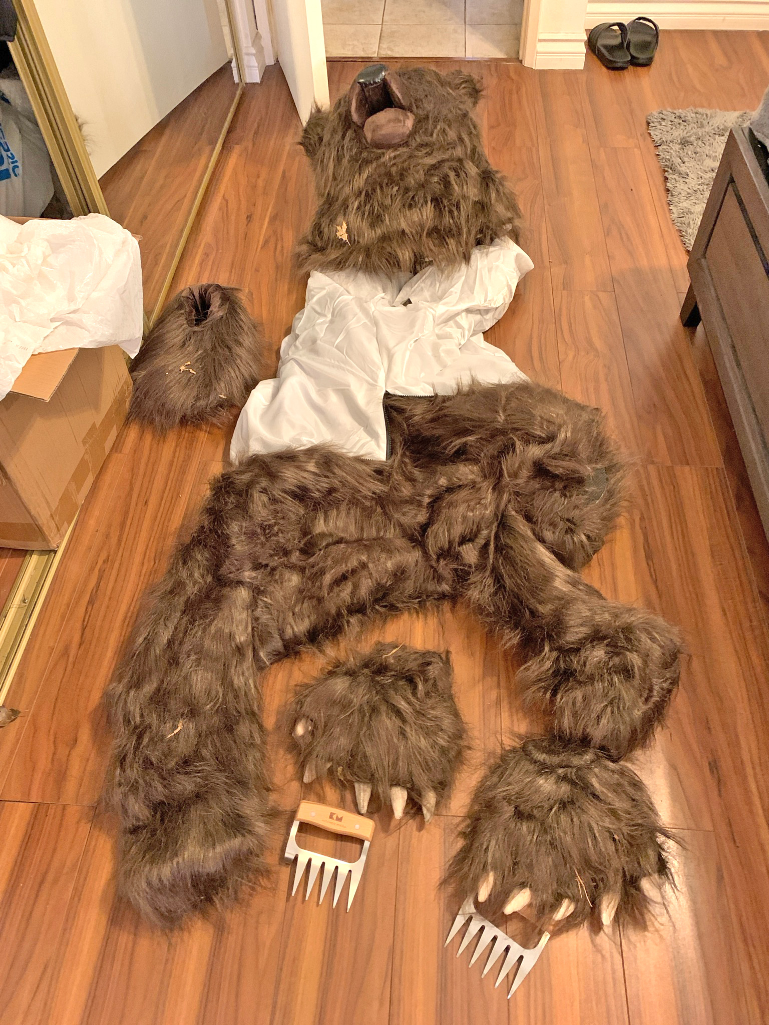 A furry, brown bear suit with metal claws laid out on a wood floor.