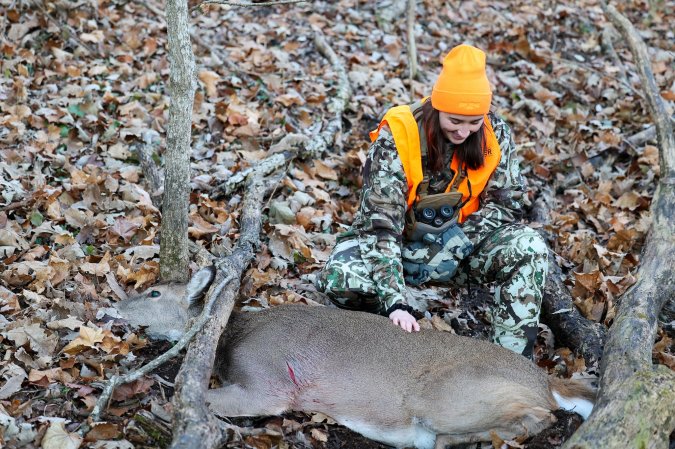 A hunter touches a dead deer on the back..