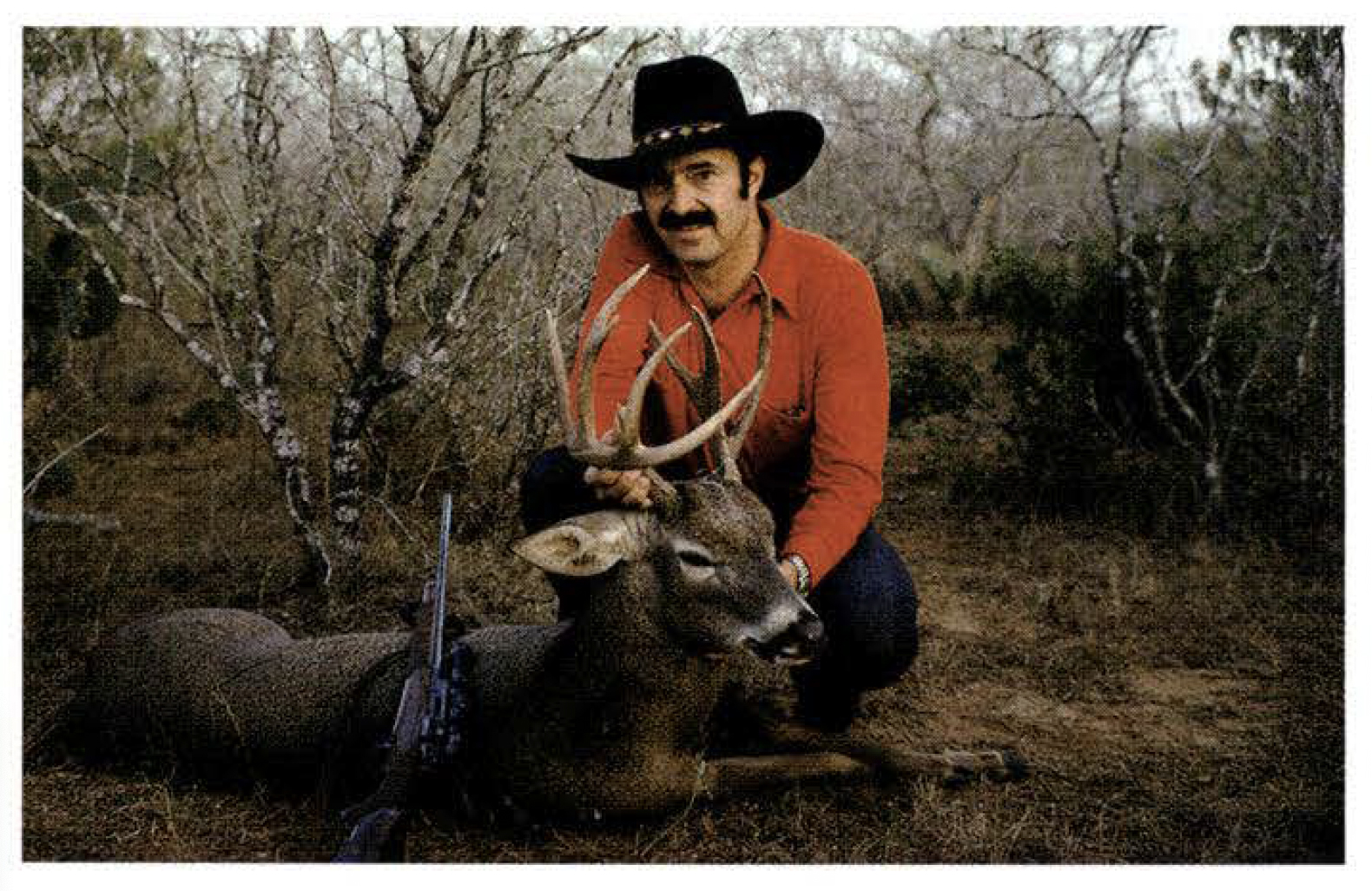 Hunter Jim Carmichel in a black hat and red shirt sitting behind a deer.