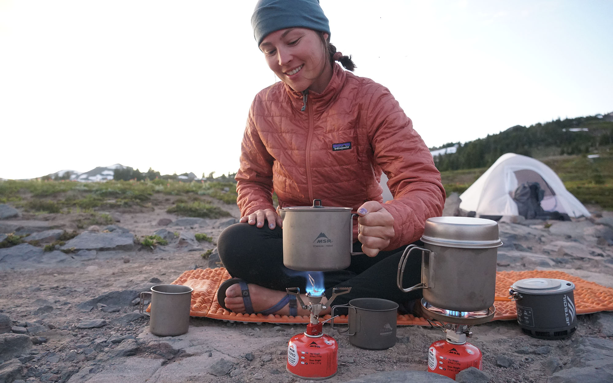 woman boiling water over two backpacking stoves in the alpine