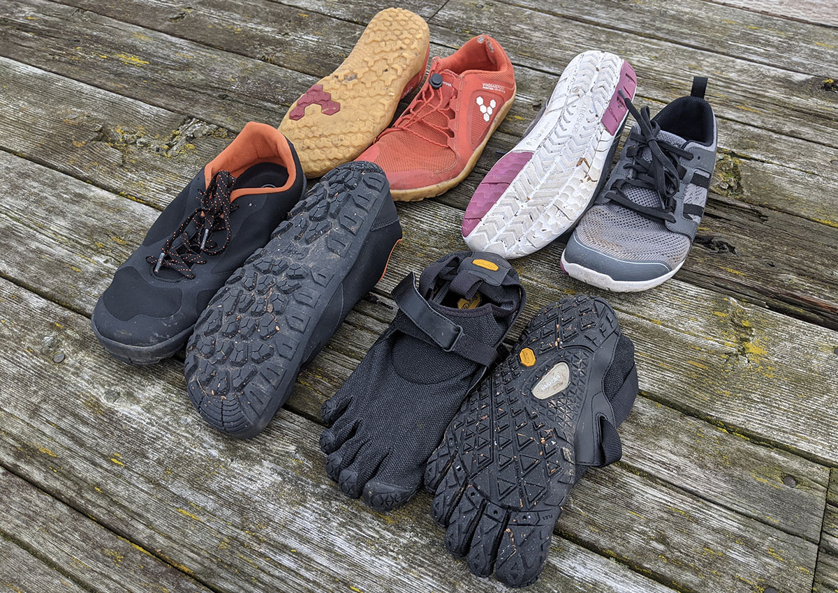 four pairs of barefoot shoes on a wooden floor with one shoe facing up one shoe facing down