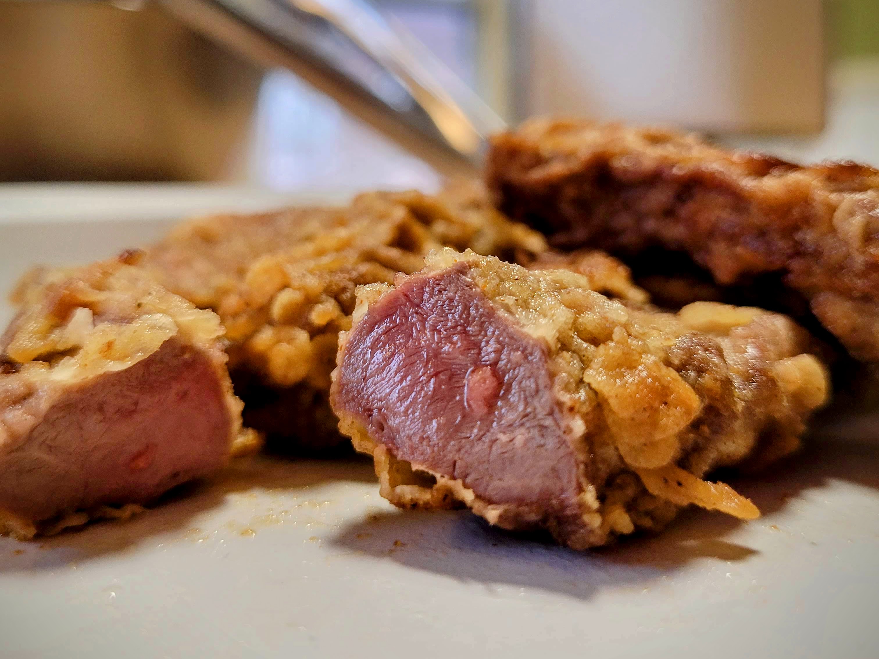 A cut of chicken-fried meat that is cut open to reveal a juicy, pink center