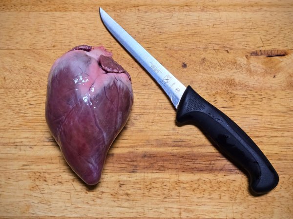 A venison heart on a wooden cutting board beside a stainless steel filet knife.