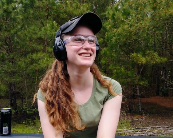 A girl wearing shooting ear pro and eye protection smiles at the camera