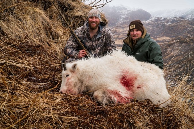 Two hunters pose with a mountain goat