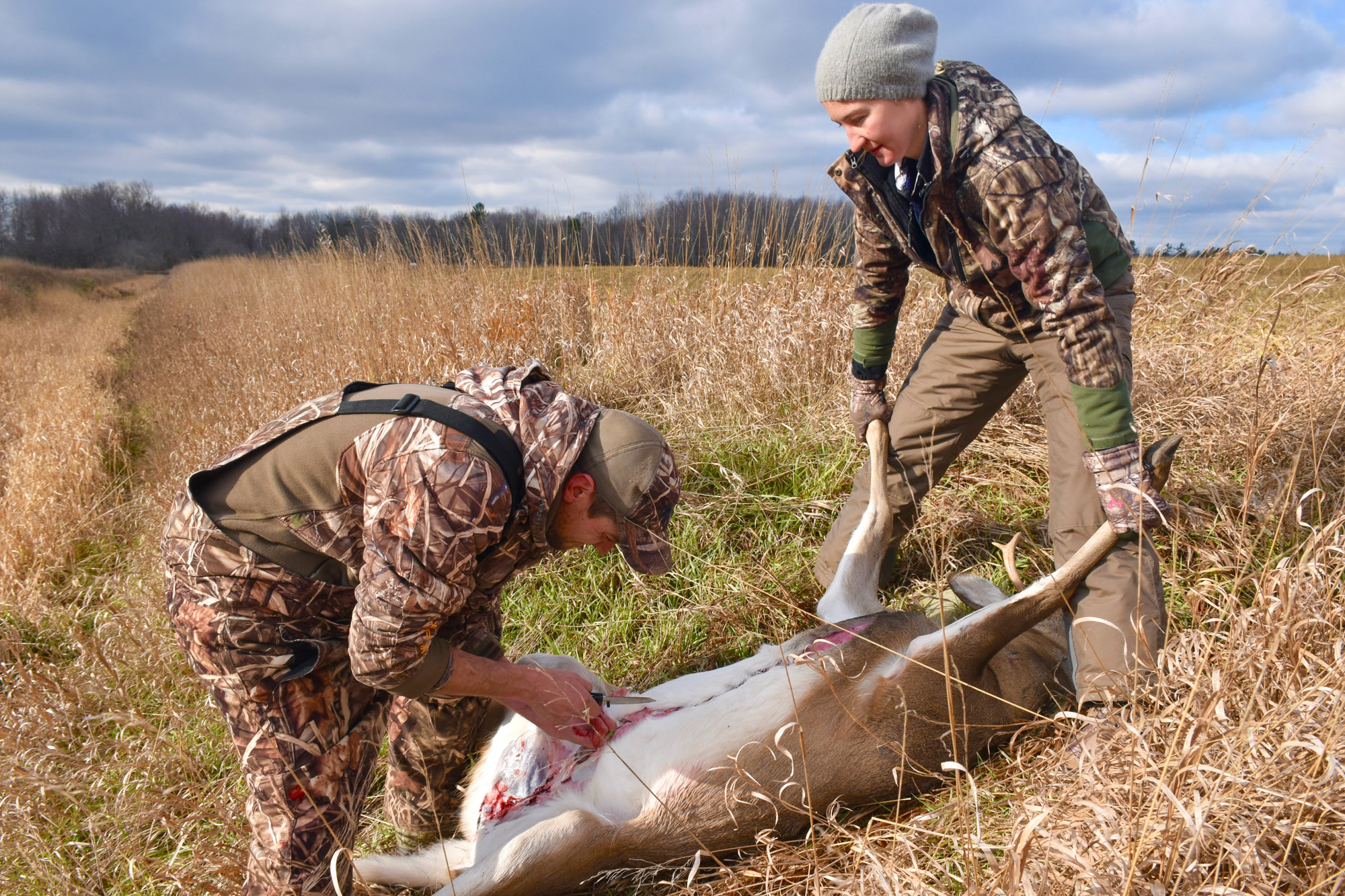 A deer hunter guts a deer while a buddy holds the two front legs.