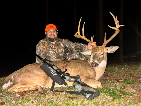 A hunter holds up a buck with stickers on its rack.