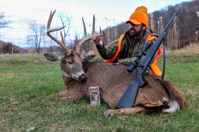 A rifle hunter sits behind a nice buck.