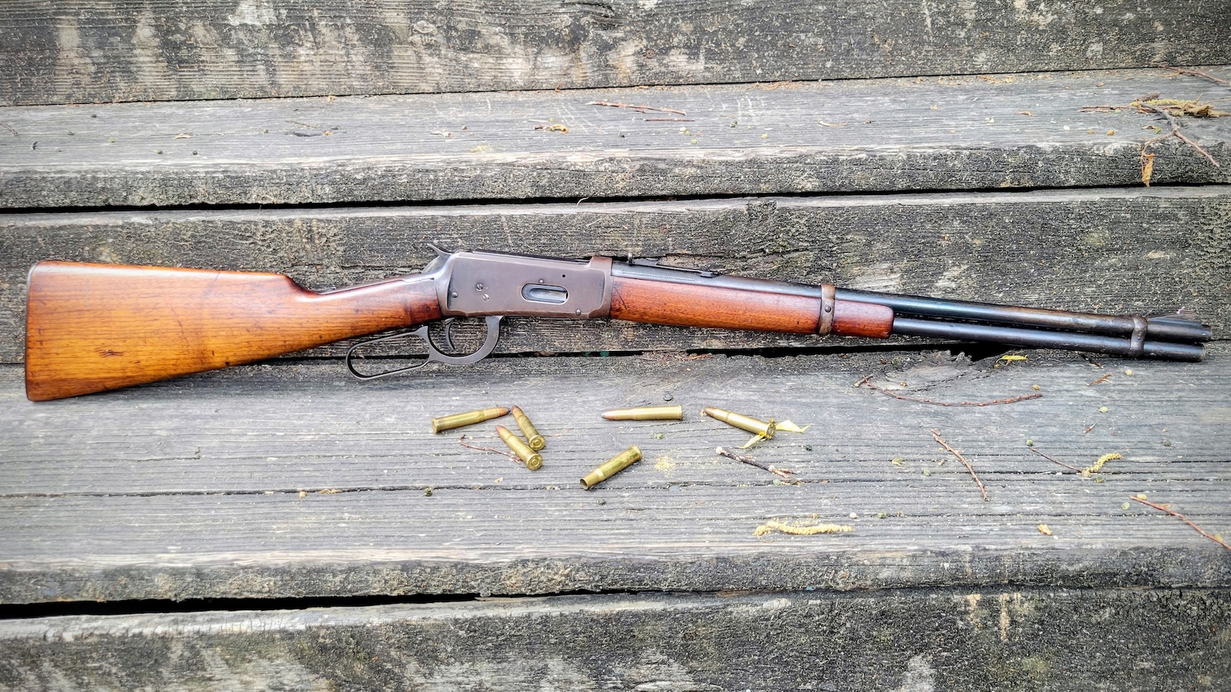 A scratched up Winchester 94 and some loose rounds lay against some old wooden boards.