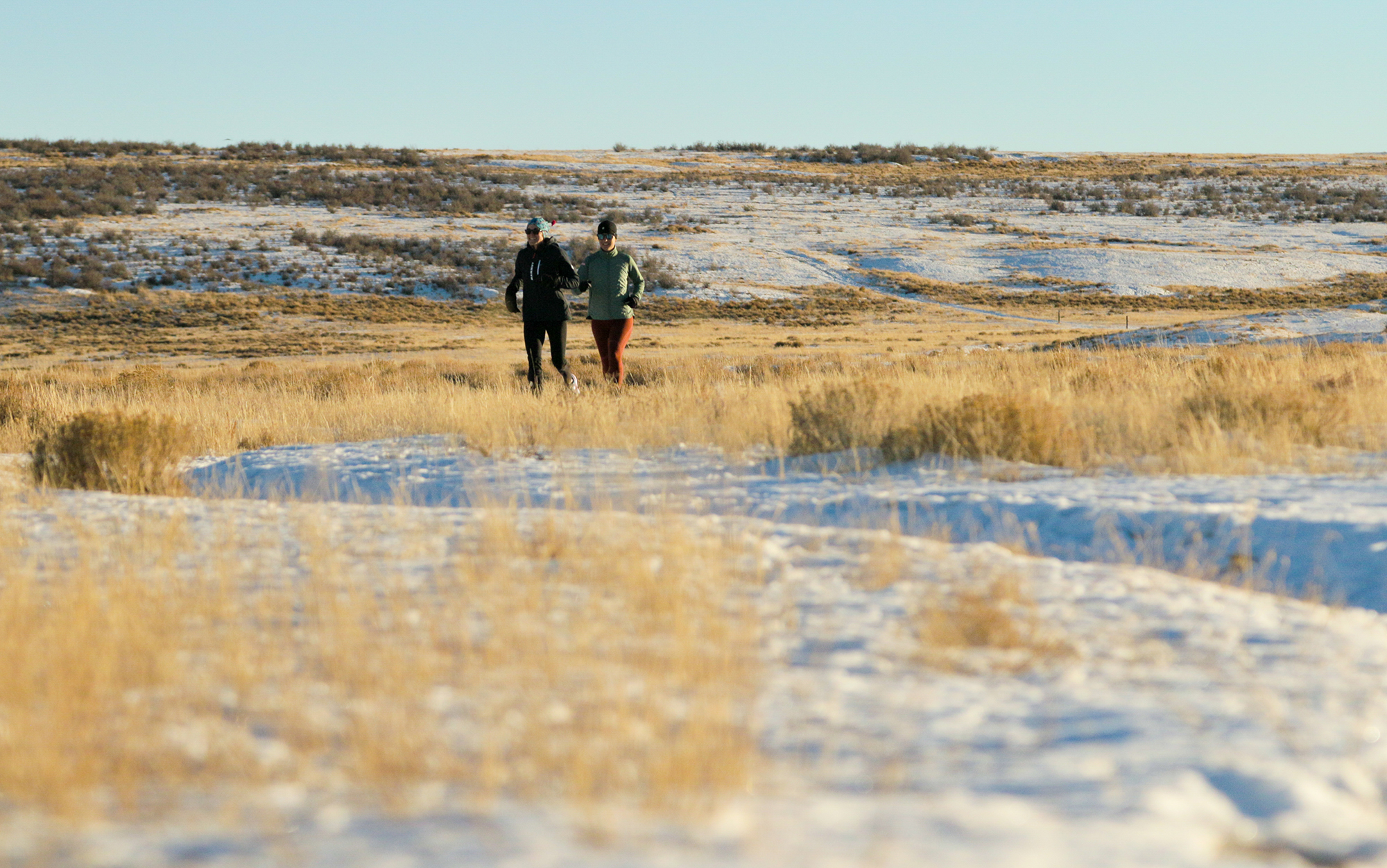 Two women run in the snow.