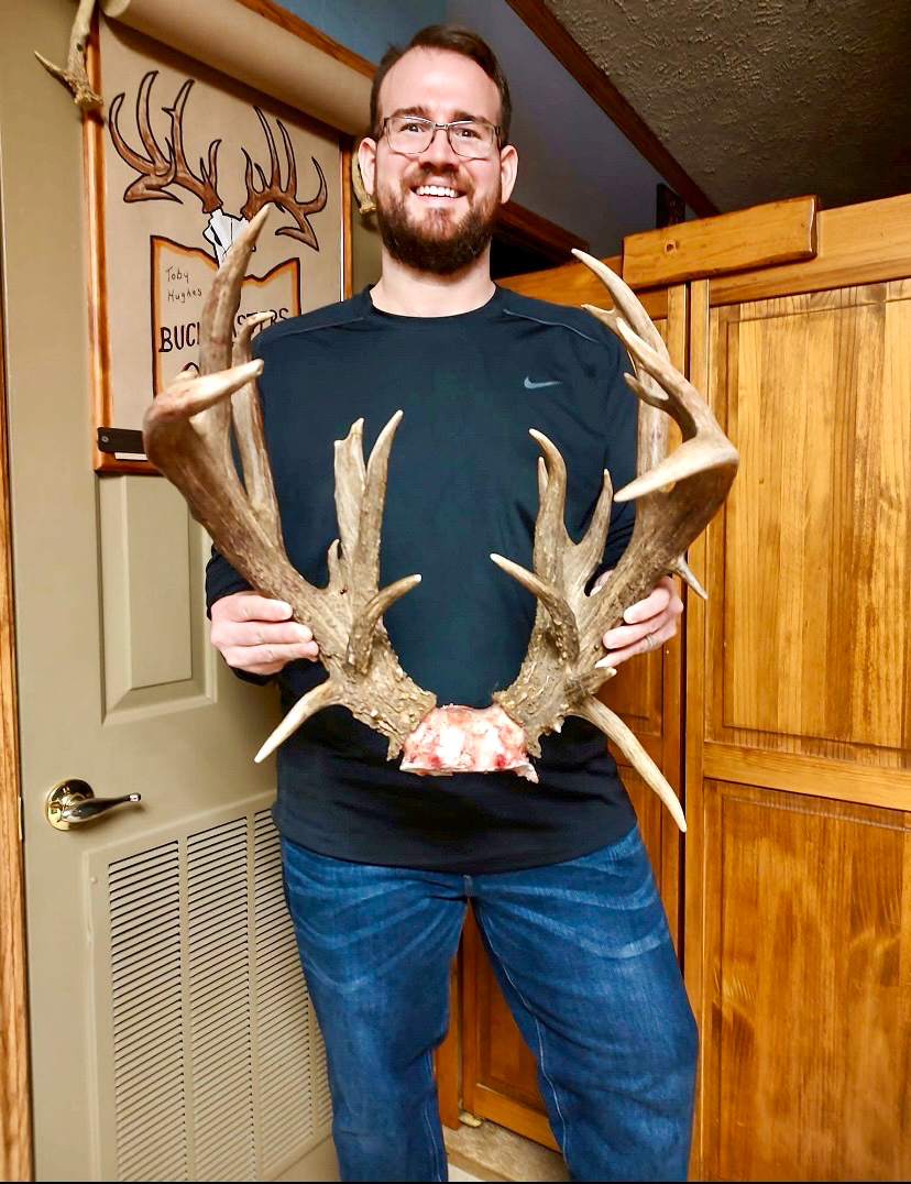 A man in a room holds antlers that were skull capped.