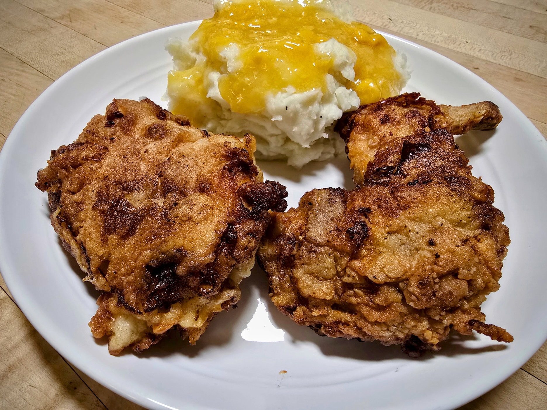 Two pieces of golden fried rabbit sit on a white dinner plate next to a pile of mashed potatoes.