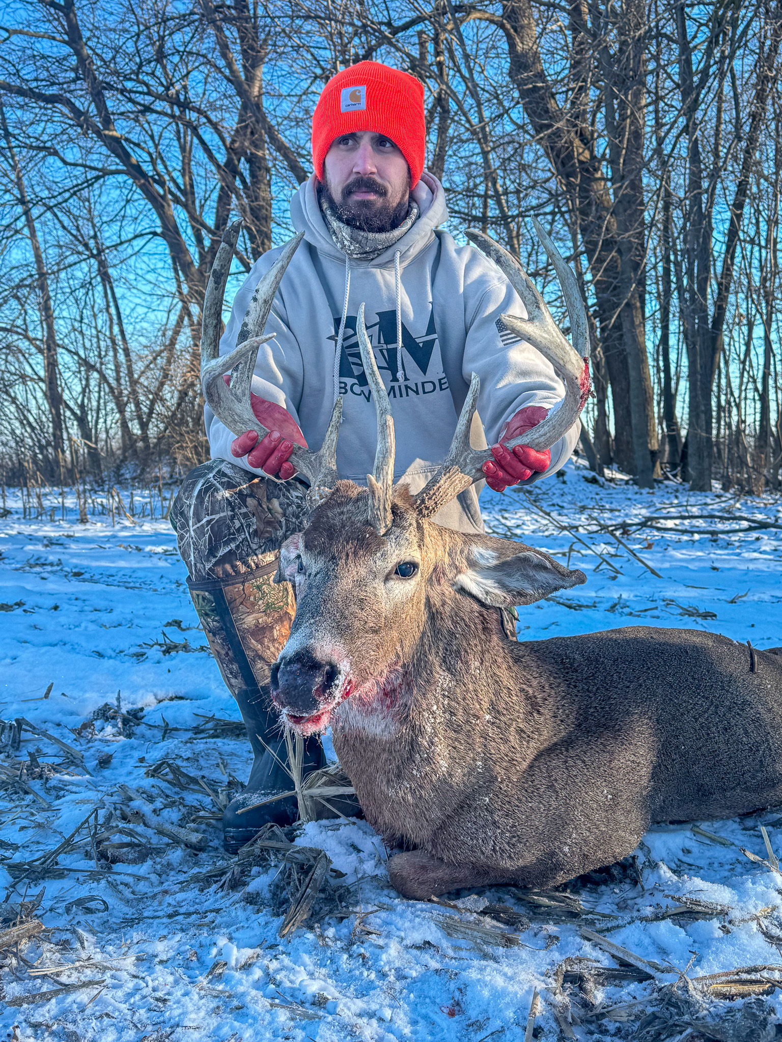 A hunter in an orange hat in the snow with a nice unicorn buck.