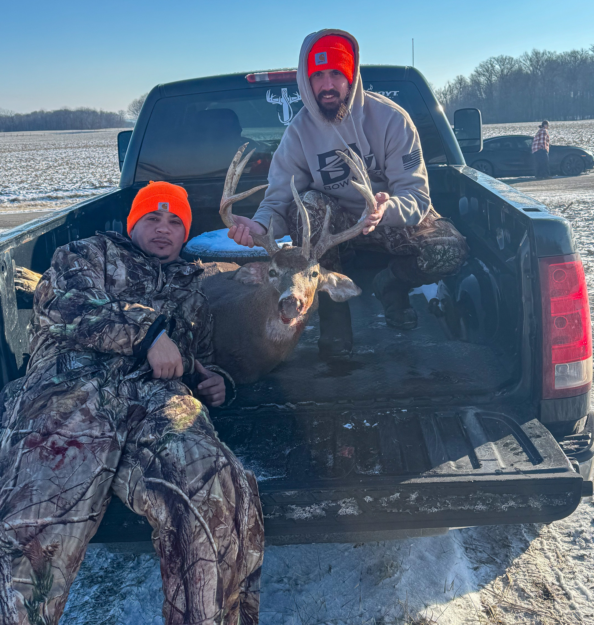 Two hunters in the back of a pickup with a nice buck.