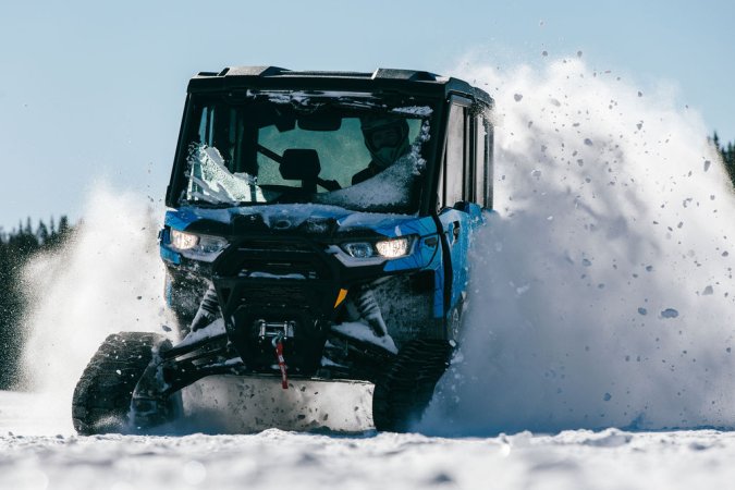 A blue Can-Am Defender with snow tracks kicks up some fresh powder.