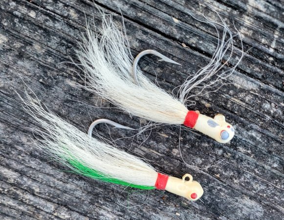 Two vintage white bucktail jigs lay on a gray wooden plank.