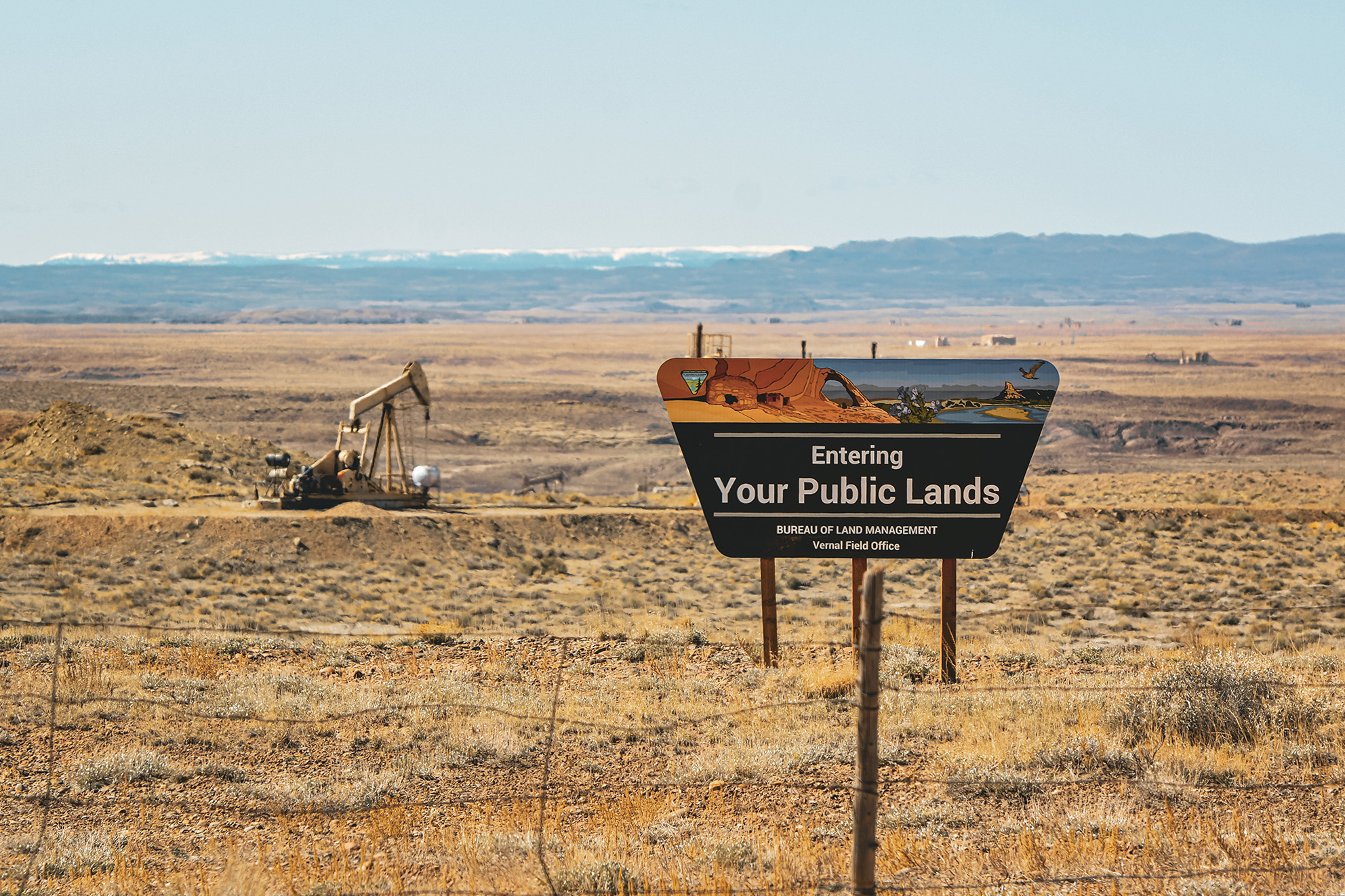 A public land sign with a pumpjack in the background.