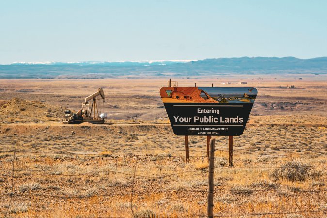 A public land sign with a pumpjack in the background.