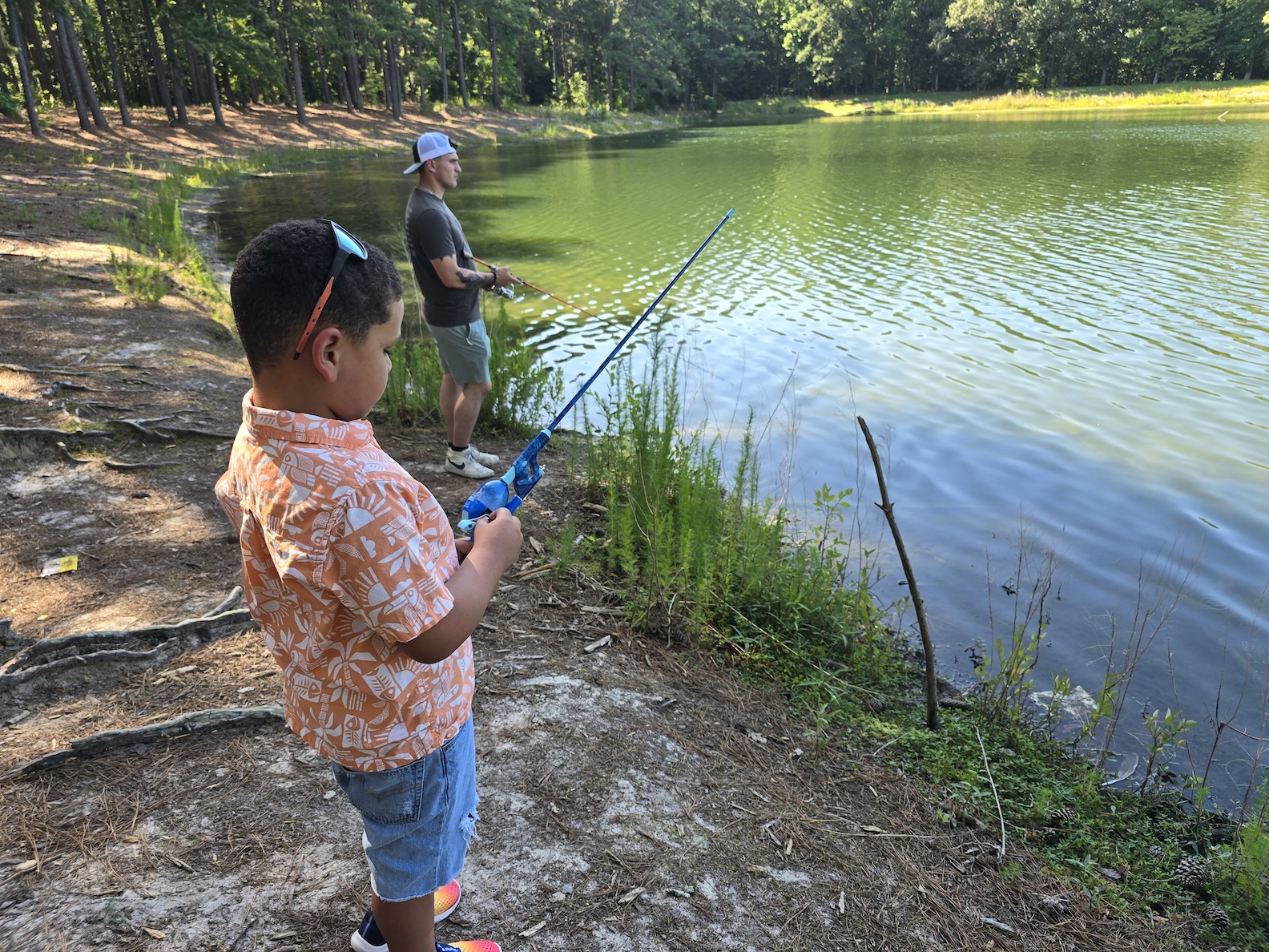 A child in an orange shirt fishes with a blue kid's fishing pole