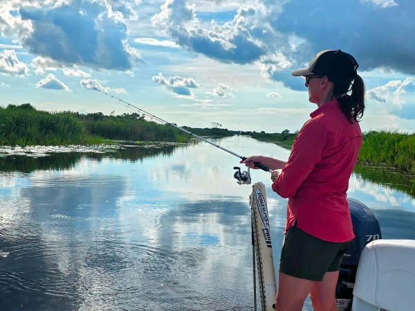 A woman fishes on a lake with a spinning rod and reel combo.