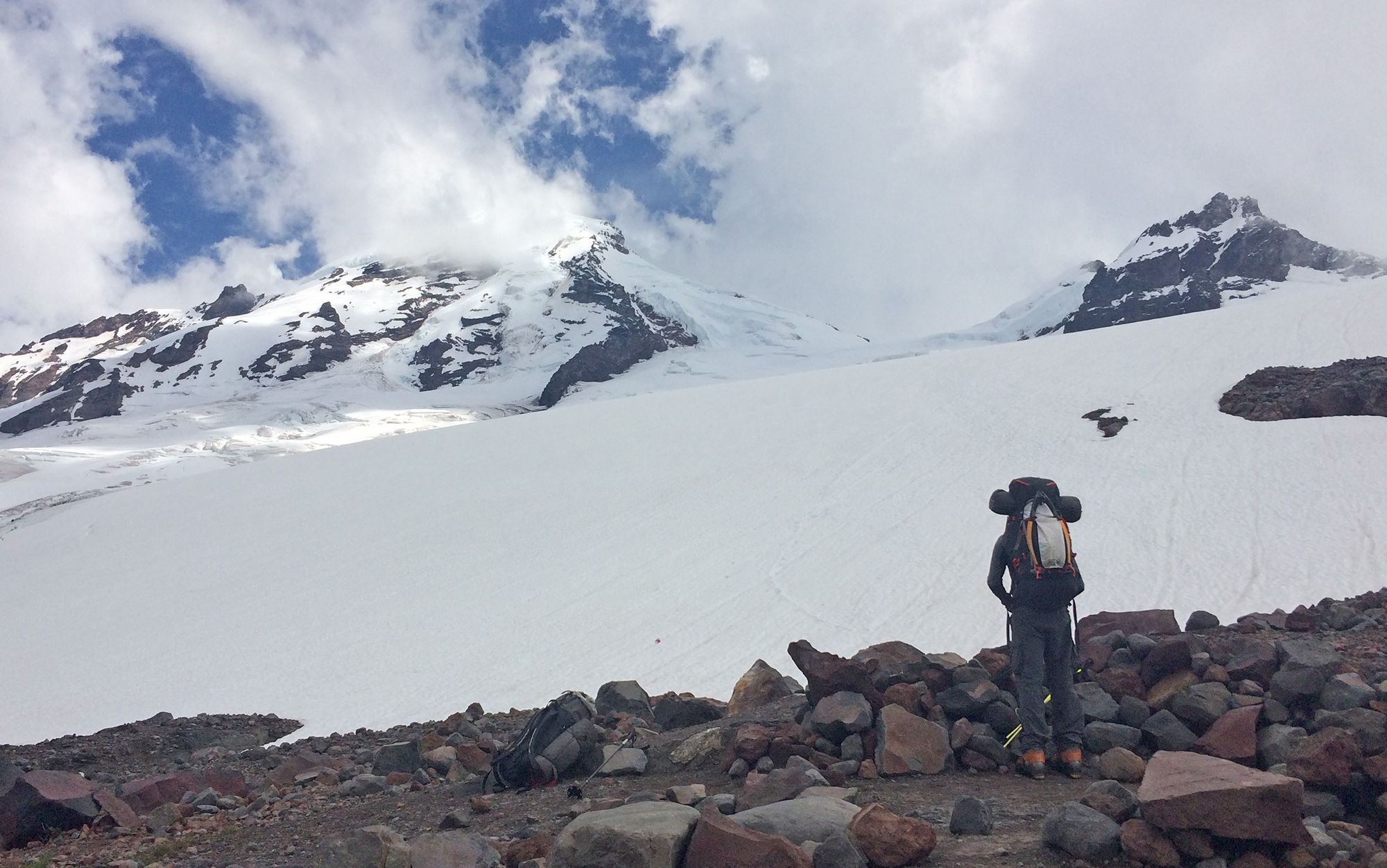 Climber wearing a backpack stands in front of a mountain.