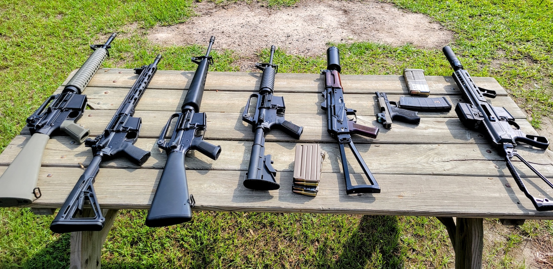 Six semi-automatic rifles and a semi-auto handgun with detachable magazines lined up on a table.