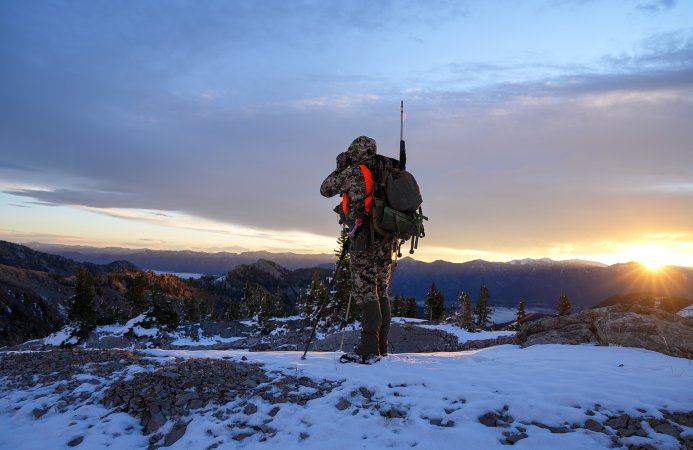 A hunter glasses for game from atop a snowy ridge.